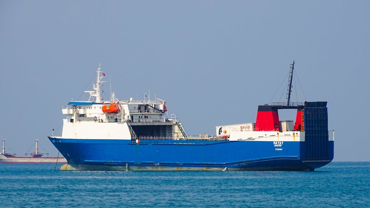 gallery-5 A large blue cargo ship navigating the calm ocean waters under a clear sky.